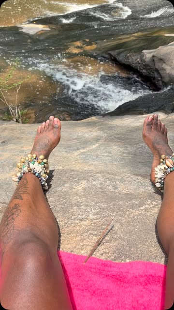 Cowrie-shell and Tibetan-bell anklets she beads herself, worn at the water